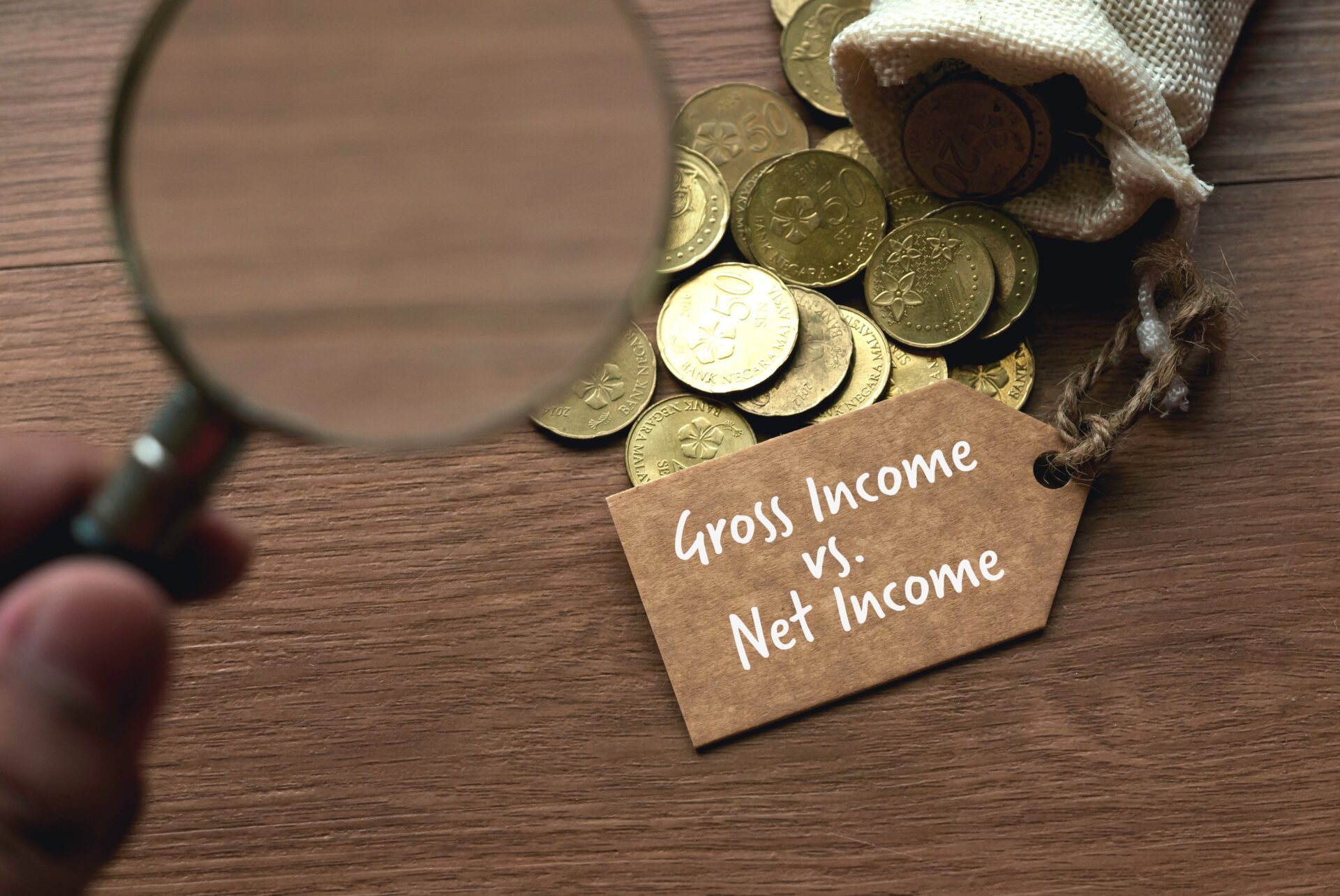 a person using a magnifying glass to learn gross income and net income.