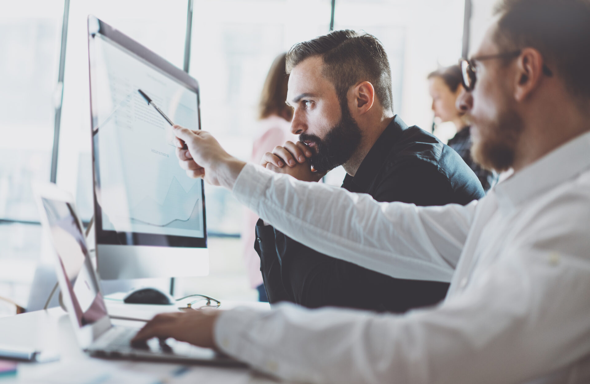 Two business men studying a computer. One is explaining invoice factoring services to the other.